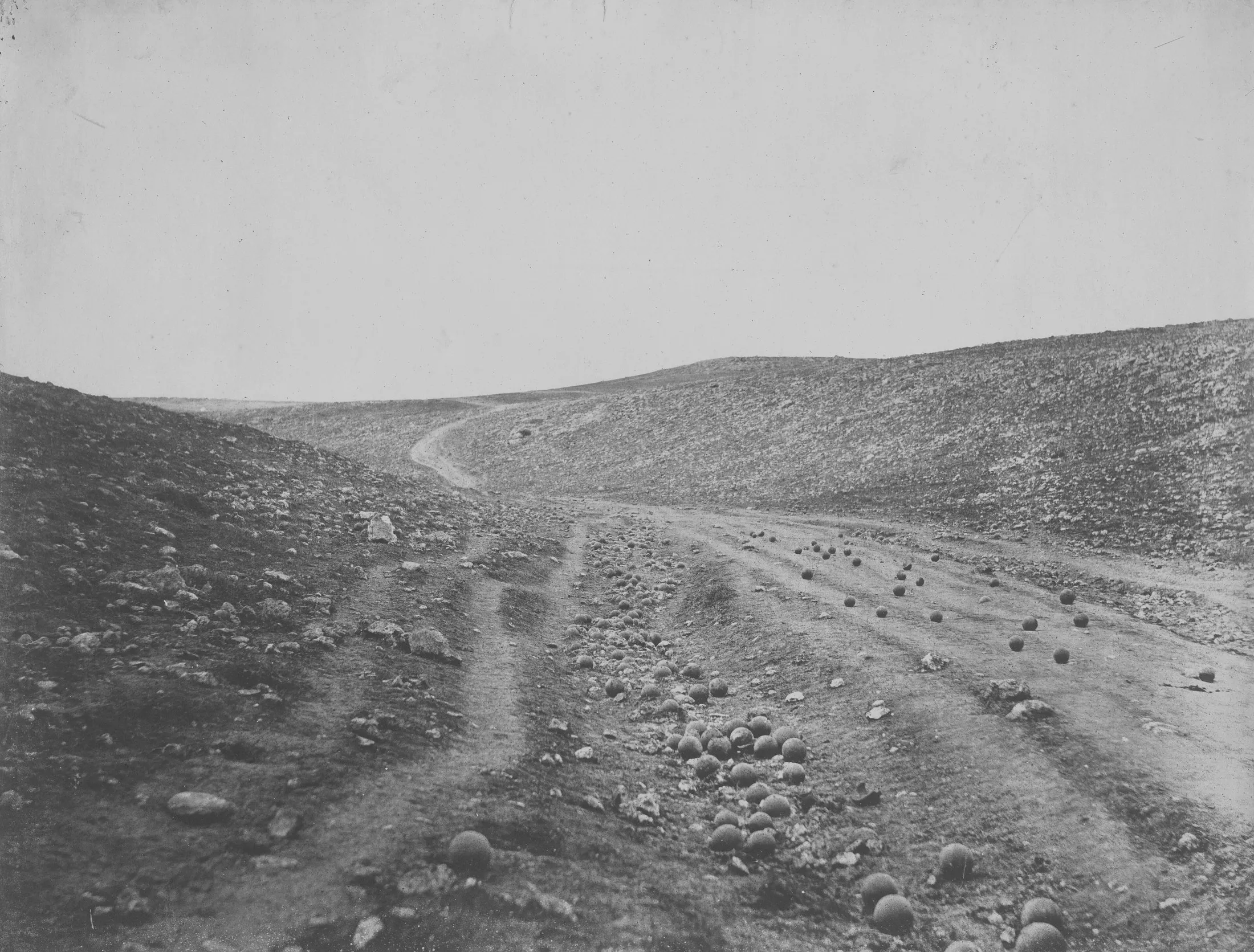 A bare, rutted road through a ravine, scattered with dozens of cannonballs.