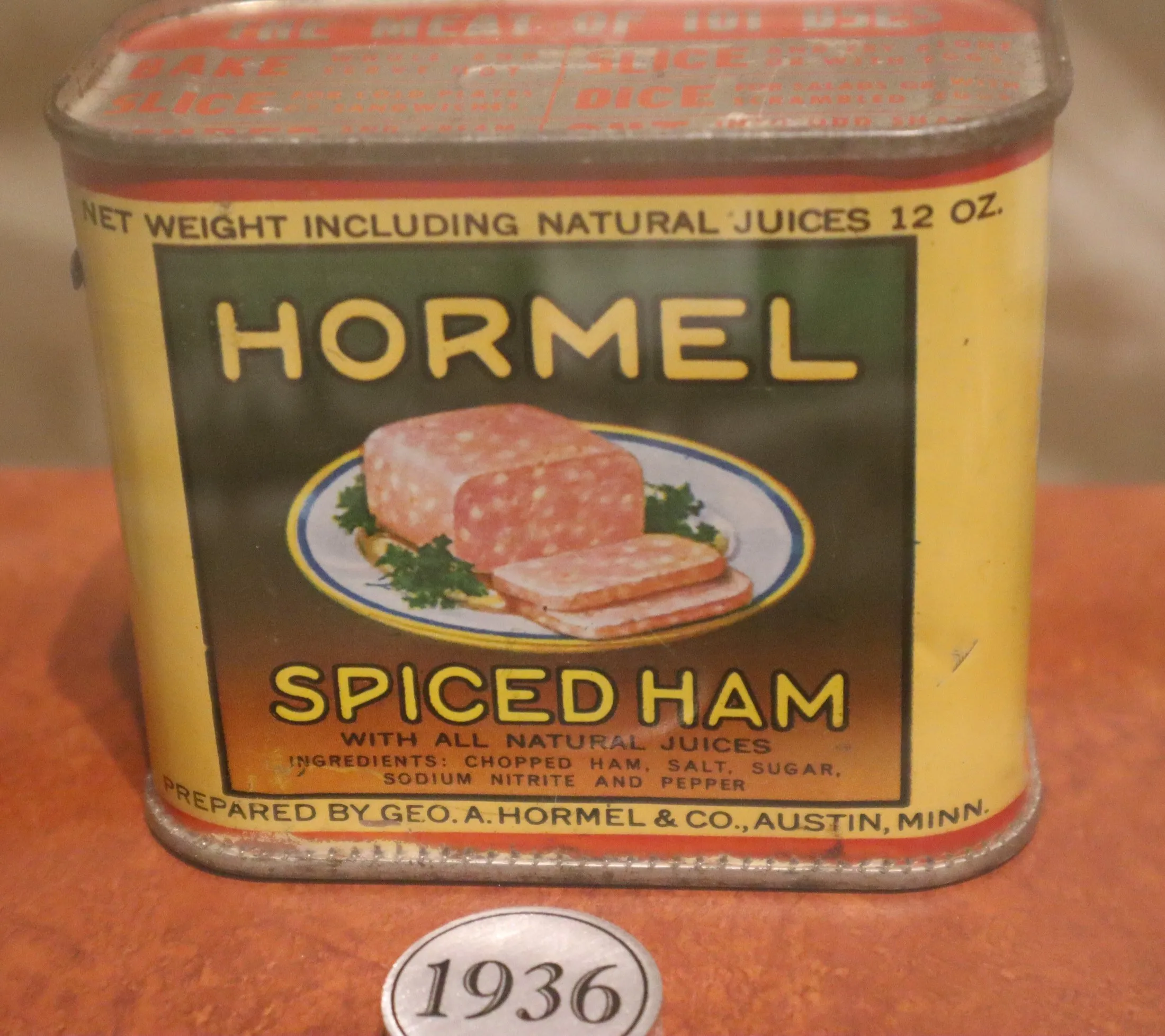 A rectangular tin with a yellow and blue label reading Hormel Spiced Ham, on a museum shelf.